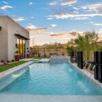 Custom backyard design with metal scupper water feature into blue pool and deco-tile, raised spa.