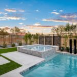 Custom backyard design with metal fencing, blue pool and artificial grass.