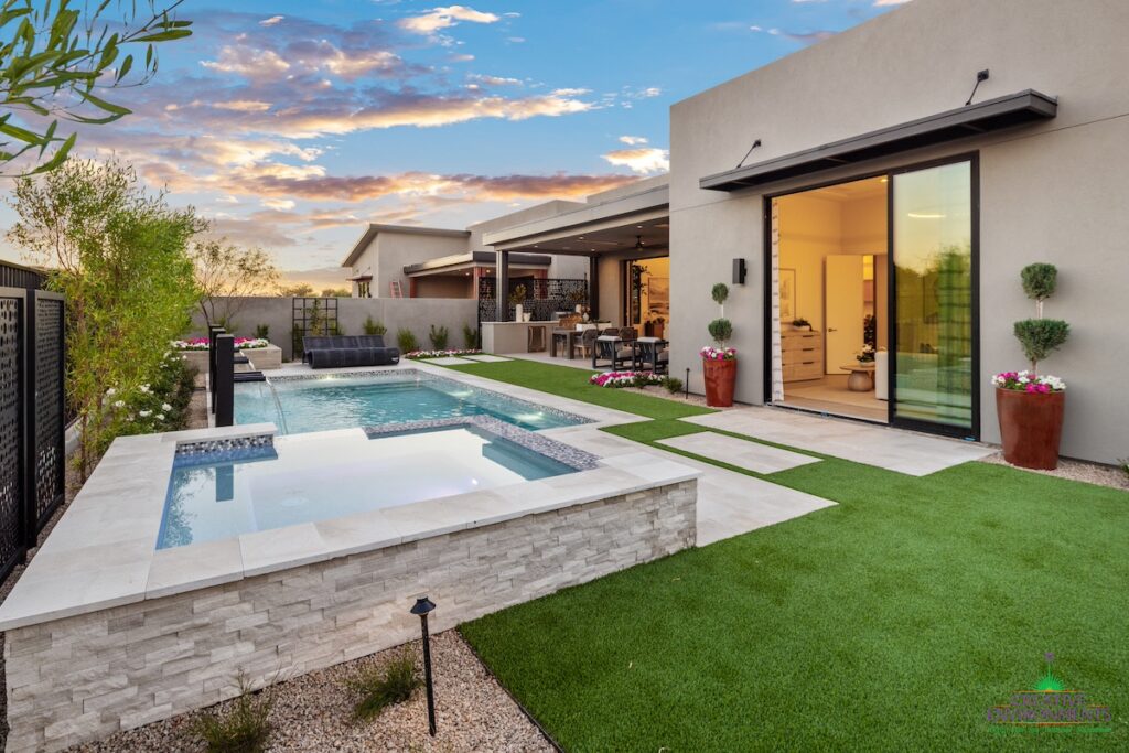 Custom backyard design with artificial grass, raised spa and blue pool.