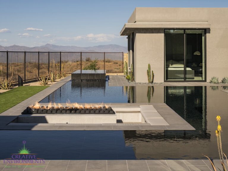 Custom backyard design with sunken fire table with fireballs, zero-edge pool and artificial grass.