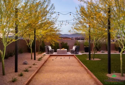 Custom backyard design with bocce ball court, string lights and square fire pit with outdoor seating area.