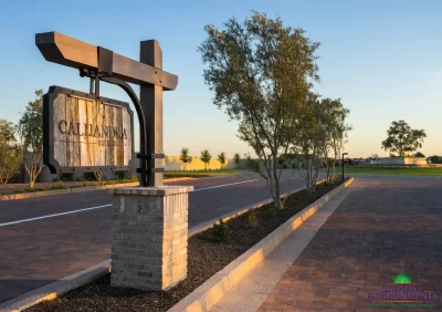 Custom community entrance with hanging sign, mixed material driveway and large water fountain.