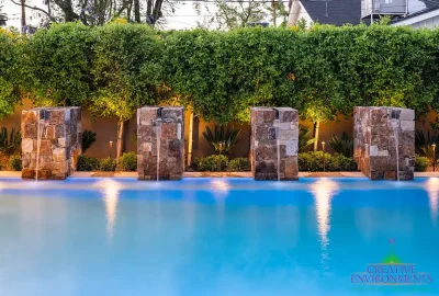 Custom backyard design with privacy hedges and natural stone water columns into pool.