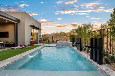 Custom backyard design with metal scupper water feature into blue pool and deco-tile, raised spa.