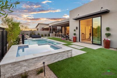 Custom backyard design with artificial grass, raised spa and blue pool.