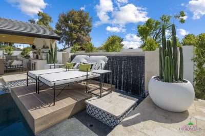Custom backyard design with black water wall, large potted plants and multiple seating areas.