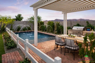 Custom backyard design with white slatted shade structure, water feature into blue pool and outdoor dining area.