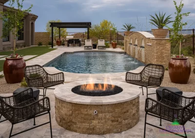 Custom backyard design with circular fire pit, slatted metal shade structure and water feature into pool.