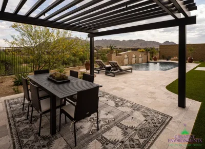 Custom backyard design with slatted metal shade structure, artificial turf and multiple seating areas.