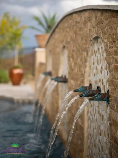 Custom backyard design with metal scupper water feature into unique-shaped pool with tile backsplash.