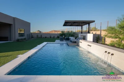 Custom backyard design with metal scupper water feature into blue pool, cantilevered shade structure and artificial turf.