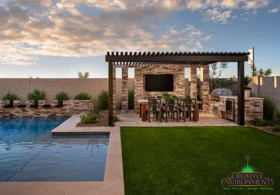 Custom backyard design with slatted metal shade structure, outdoor kitchen with dining area and metal scupper water feature into a blue pool.