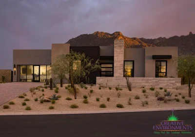 Custom front yard design with paver driveway, organized planting and natural stone privacy wall.