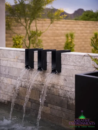 Custom backyard design with metal scupper water feature, pool retention wall and desert plants.