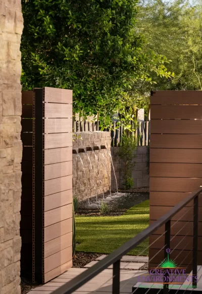 Custom side yard design with wooden door, water feature and metal fencing.
