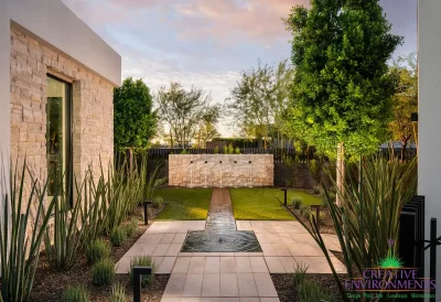 Custom backyard design with water feature, up lighting and artificial turf.