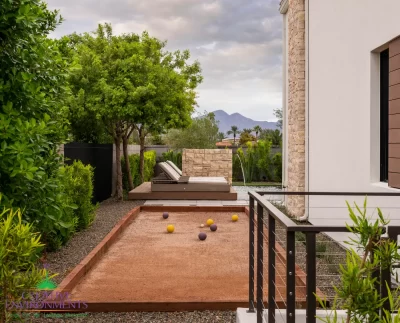 Custom backyard design with bocce ball court, privacy hedges and metal fencing.