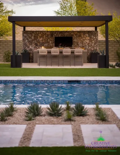 Custom backyard design with blue pool, angled shade structure and large metal planters.