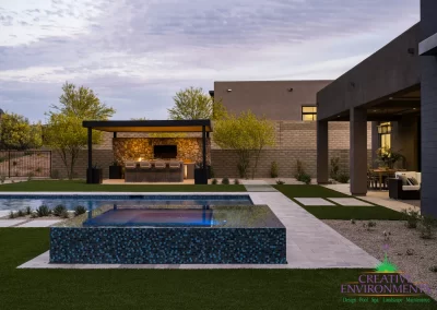 Custom backyard design with blue raised spa, artificial turf and metal shade structure.