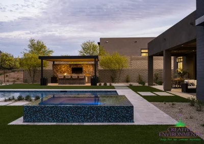 Custom backyard design with blue raised spa, artificial turf and metal shade structure.