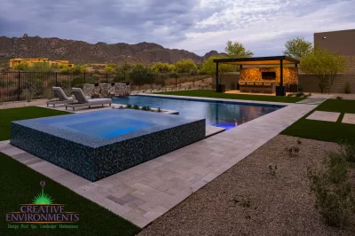 Custom backyard design with natural stone decking, blue raised spa and metal shade structure.