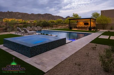 Custom backyard design with natural stone decking, blue raised spa and metal shade structure.
