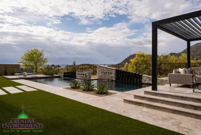 Custom backyard design with multiple water features, raised outdoor entertainment area and artificial turf.
