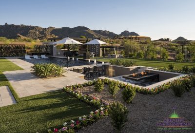 Custom backyard design with sunken entertainment area with cantilevered fire table, large, black pool and artificial grass.