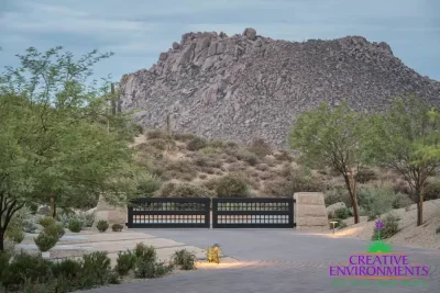 Custom front metal entry gate with desert plants, brick roundabout driveway and up lighting.