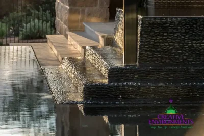 Custom black pebble stone water feature into pool.