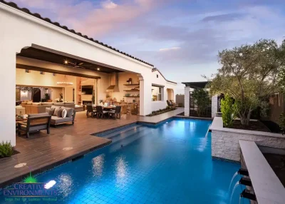 Custom backyard design with natural stone accents, blue pool and privacy hedges.