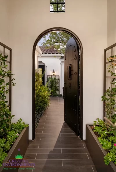 Custom front entryway with metal trellis, arched doorway and greenery.