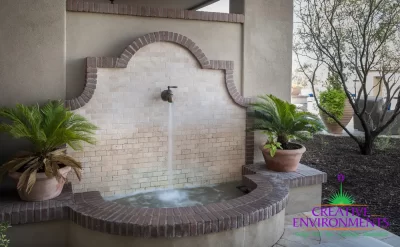 Custom backyard design with planters, faucet water feature and Spanish design style.
