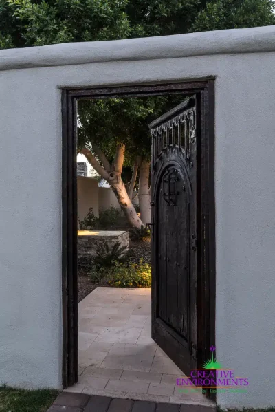 Custom metal entry gate with travertine devking and large tree.