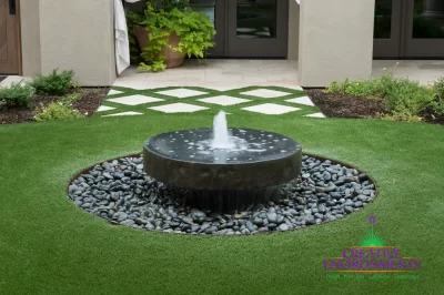 Custom courtyard design with black water feature, artificial turf pattern and black beach pebble stones.