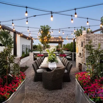 Custom backyard design with string lights, outdoor dining area and multiple planters filled with annuals and small trees.