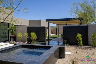 Custom backyard design with metal shade structure, raised spa and metal privacy gate.